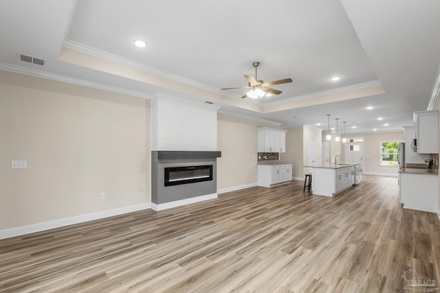 unfurnished living room featuring light wood finished floors, a sink, visible vents, a ceiling fan, and a raised ceiling
