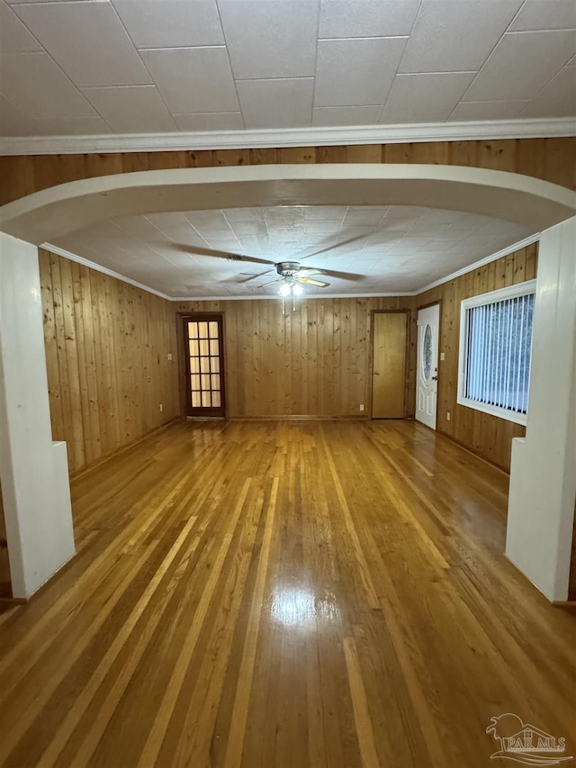 unfurnished living room with ceiling fan, wood-type flooring, and wood walls