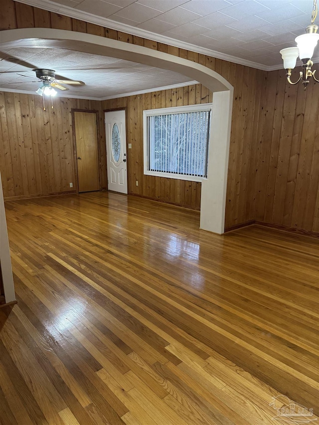 spare room with ornamental molding, wood-type flooring, wooden walls, and ceiling fan with notable chandelier