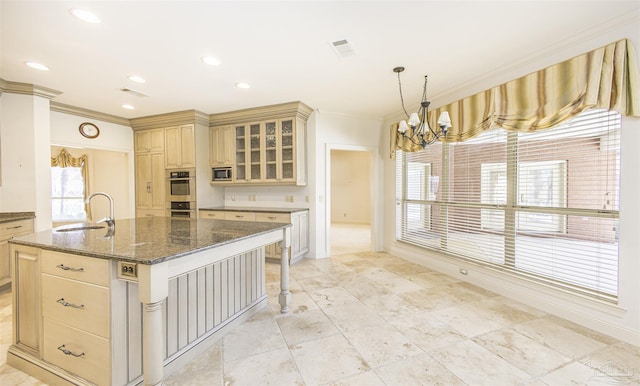 kitchen featuring sink, a chandelier, an island with sink, stainless steel double oven, and dark stone counters