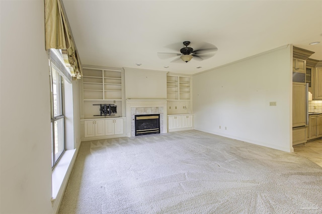 unfurnished living room with crown molding, ceiling fan, a fireplace, light carpet, and built in shelves