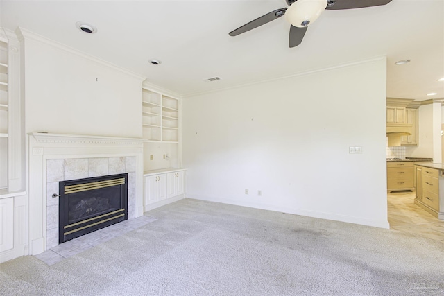 unfurnished living room featuring a tiled fireplace, crown molding, light carpet, and built in shelves