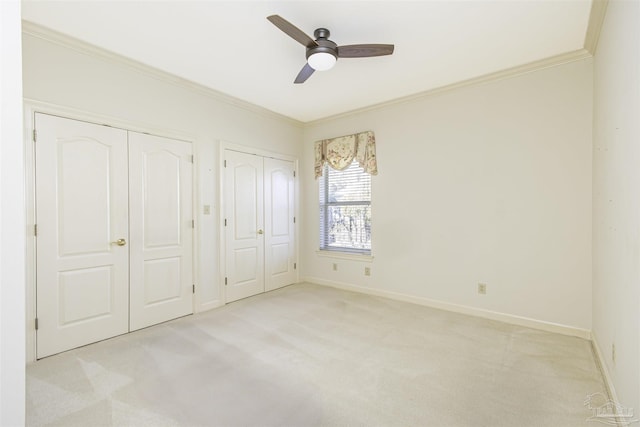 unfurnished bedroom featuring light carpet, two closets, crown molding, and ceiling fan