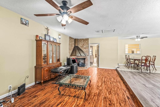 living room featuring a wood stove, ceiling fan, hardwood / wood-style floors, and a textured ceiling