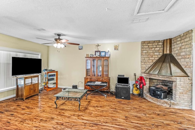 living room with a wood stove, hardwood / wood-style flooring, ceiling fan, and a textured ceiling