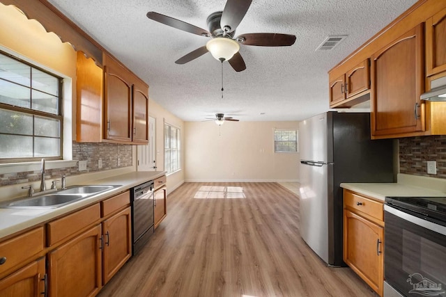 kitchen featuring backsplash, a textured ceiling, stainless steel appliances, sink, and light hardwood / wood-style flooring