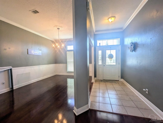 entryway with a chandelier, a textured ceiling, ornamental molding, and hardwood / wood-style floors