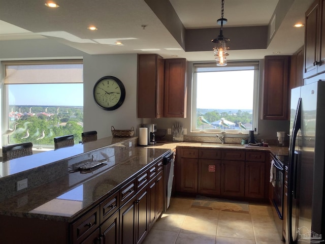 kitchen with pendant lighting, light tile patterned floors, appliances with stainless steel finishes, dark stone countertops, and a raised ceiling