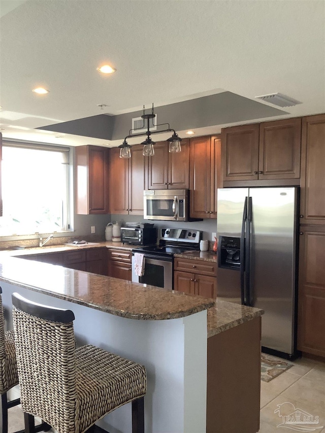 kitchen featuring stainless steel appliances, a breakfast bar, light tile patterned floors, and dark stone counters