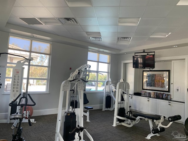 gym featuring a paneled ceiling, dark carpet, and a wealth of natural light