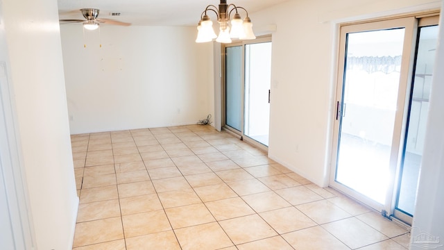 spare room featuring a healthy amount of sunlight, light tile patterned flooring, and ceiling fan with notable chandelier