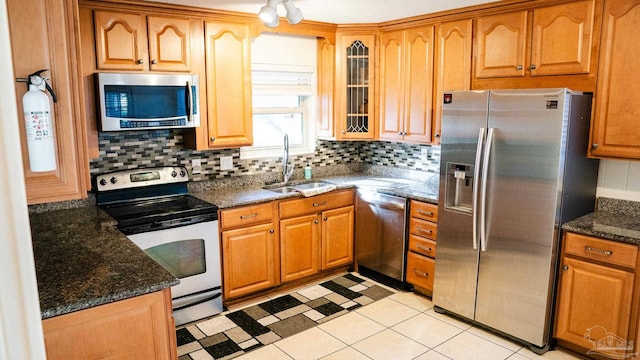 kitchen with appliances with stainless steel finishes, dark stone countertops, sink, and light tile patterned floors