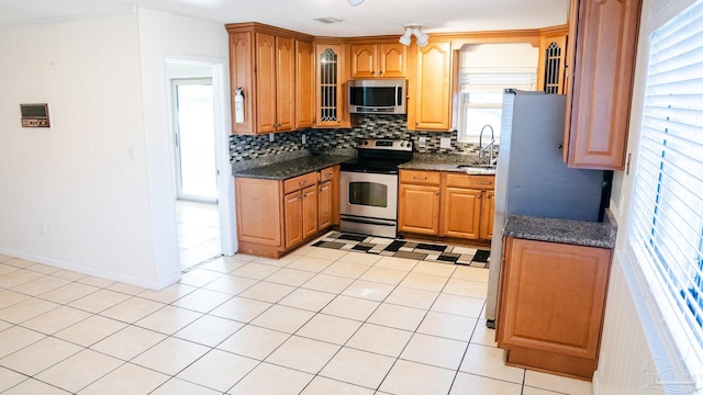 kitchen with tasteful backsplash, light tile patterned flooring, sink, stainless steel appliances, and dark stone countertops