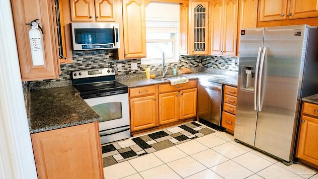 kitchen featuring dark stone counters, sink, light tile patterned floors, appliances with stainless steel finishes, and tasteful backsplash