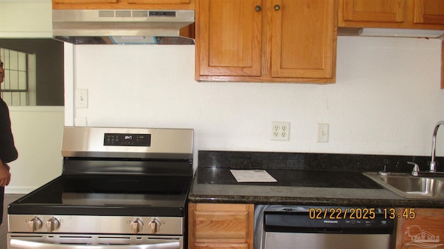 kitchen with dark countertops, appliances with stainless steel finishes, brown cabinets, under cabinet range hood, and a sink