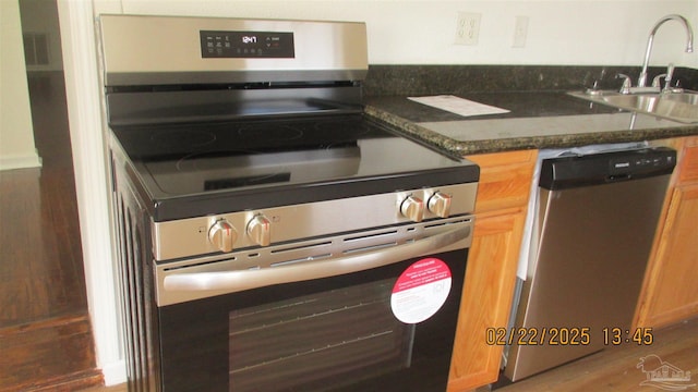 kitchen featuring appliances with stainless steel finishes, dark stone counters, brown cabinetry, and a sink