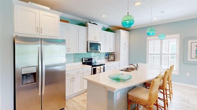 kitchen with a kitchen island with sink, white cabinets, tasteful backsplash, a sink, and appliances with stainless steel finishes