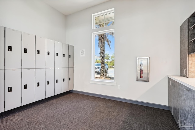 unfurnished bedroom with dark carpet, baseboards, and a towering ceiling