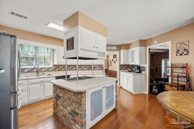 kitchen with stainless steel refrigerator, white cabinetry, sink, and a center island with sink