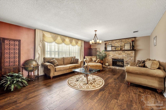 living room featuring an inviting chandelier, a brick fireplace, dark wood-type flooring, and a textured ceiling