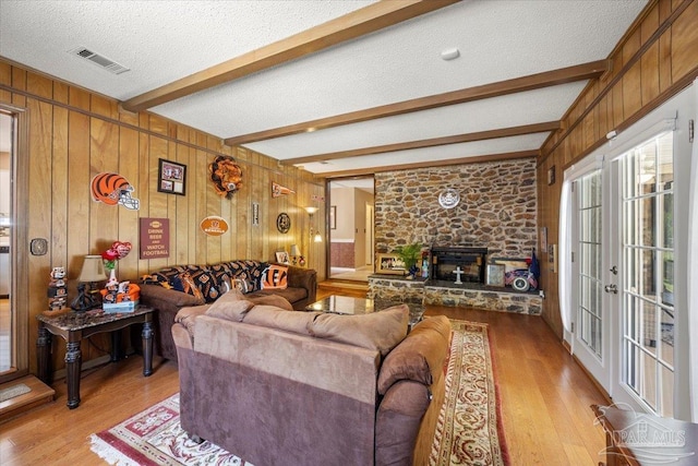 living room with beamed ceiling, a fireplace, a textured ceiling, and light hardwood / wood-style flooring