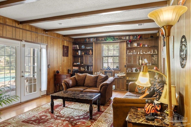 living room featuring beam ceiling, wood-type flooring, a textured ceiling, french doors, and wood walls