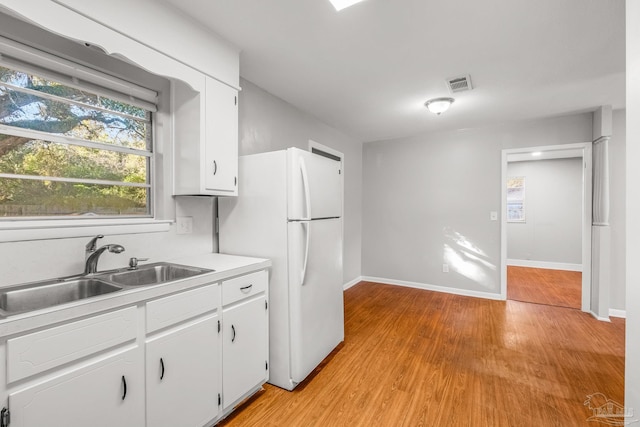 kitchen with white cabinets, white refrigerator, light hardwood / wood-style floors, and sink