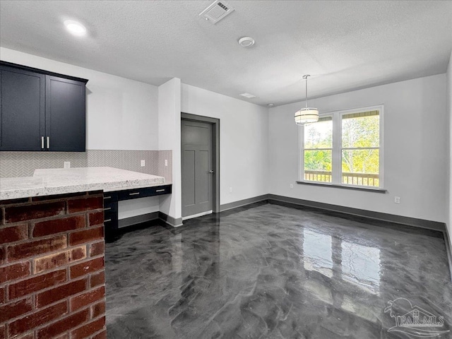 interior space featuring pendant lighting, light stone countertops, decorative backsplash, and a textured ceiling