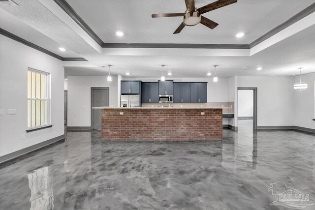 kitchen with hanging light fixtures, ceiling fan, a tray ceiling, stainless steel appliances, and a spacious island