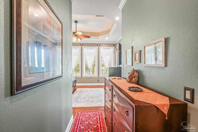 hall with crown molding, hardwood / wood-style flooring, and a tray ceiling