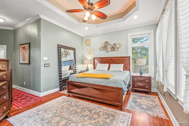 bedroom with crown molding, a raised ceiling, light hardwood / wood-style floors, and ceiling fan