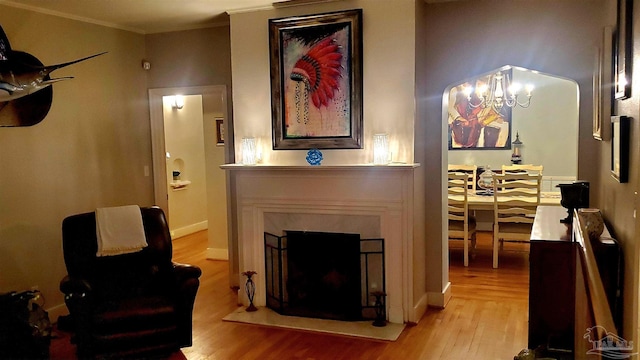 living room featuring crown molding, light hardwood / wood-style flooring, a notable chandelier, and a fireplace