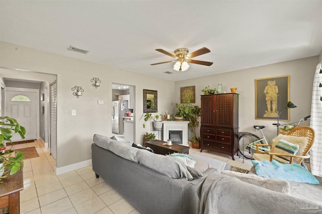 living room featuring visible vents, baseboards, ceiling fan, light tile patterned flooring, and a glass covered fireplace