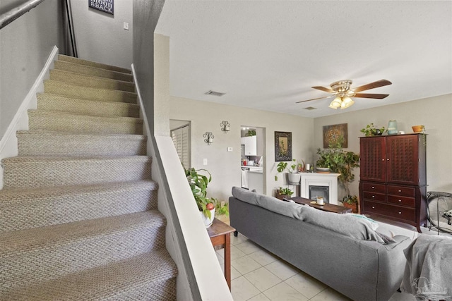 staircase with tile patterned floors, visible vents, a fireplace, and a ceiling fan