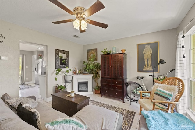 living room featuring light tile patterned floors, baseboards, visible vents, ceiling fan, and a glass covered fireplace