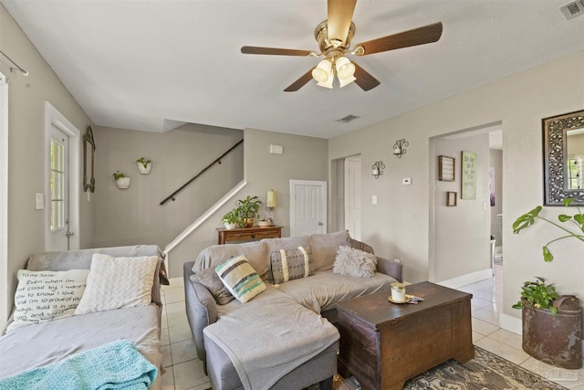 living area with light tile patterned floors, visible vents, ceiling fan, and stairway