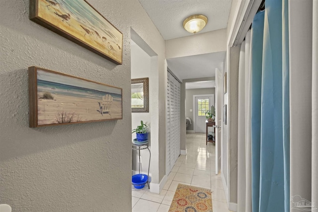 hallway with light tile patterned flooring, a textured wall, baseboards, and a textured ceiling