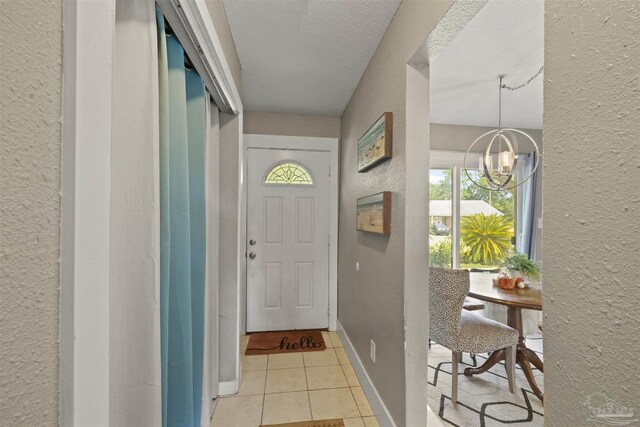 entryway with baseboards, a chandelier, light tile patterned floors, a textured wall, and a textured ceiling