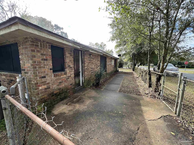 view of side of home featuring brick siding, fence, and a patio