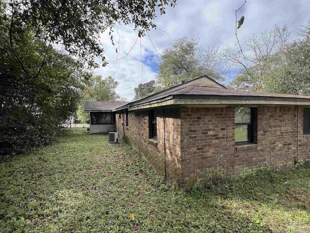 view of property exterior with a sunroom, brick siding, a lawn, and central air condition unit