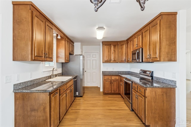 kitchen with light wood-type flooring, sink, appliances with stainless steel finishes, and dark stone counters