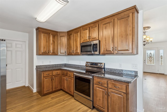 kitchen featuring appliances with stainless steel finishes, light wood-type flooring, dark stone counters, and a notable chandelier