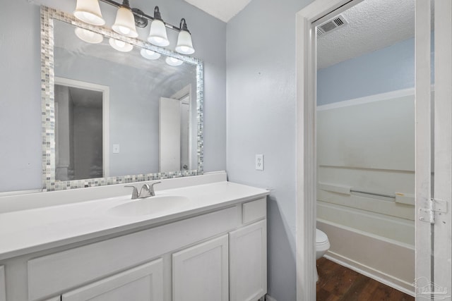 full bathroom with washtub / shower combination, wood-type flooring, a textured ceiling, toilet, and vanity