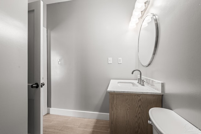 bathroom with toilet, vanity, baseboards, and wood finished floors