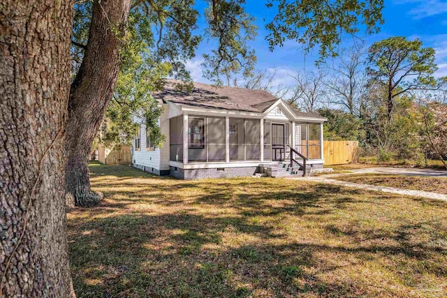 view of front facade featuring a sunroom, roof with shingles, crawl space, fence, and a front lawn