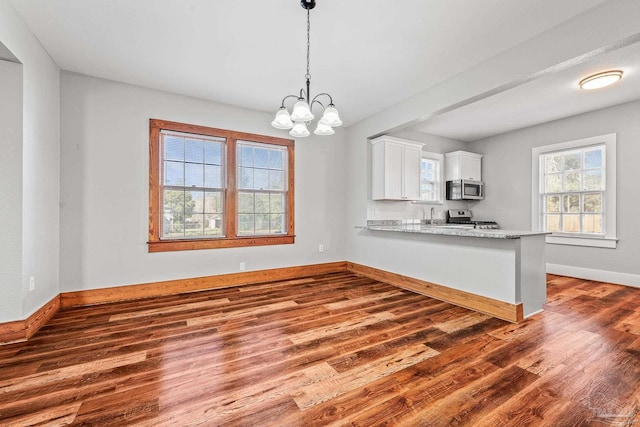 kitchen with stainless steel appliances, hanging light fixtures, white cabinetry, wood finished floors, and baseboards