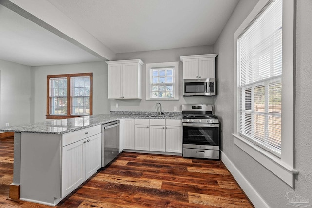 kitchen featuring light stone counters, a peninsula, dark wood-type flooring, white cabinetry, and appliances with stainless steel finishes