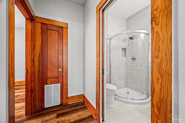 full bathroom featuring visible vents, toilet, a shower stall, wood finished floors, and baseboards