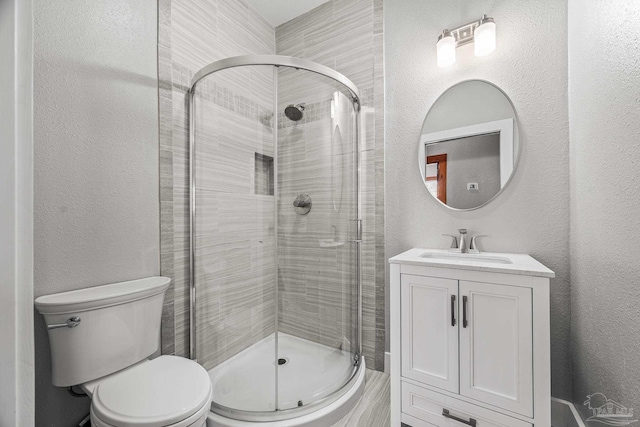 bathroom with toilet, a shower stall, vanity, and a textured wall