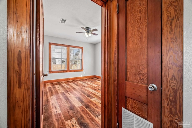 unfurnished room with a ceiling fan, visible vents, baseboards, and wood finished floors